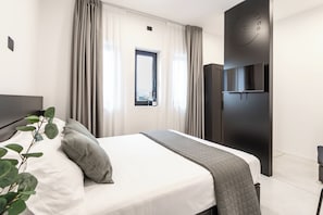 A modern bedroom with a large bed, a TV mounted on a dark wall, and a window with curtains. - Feudo Antico (Tollo)