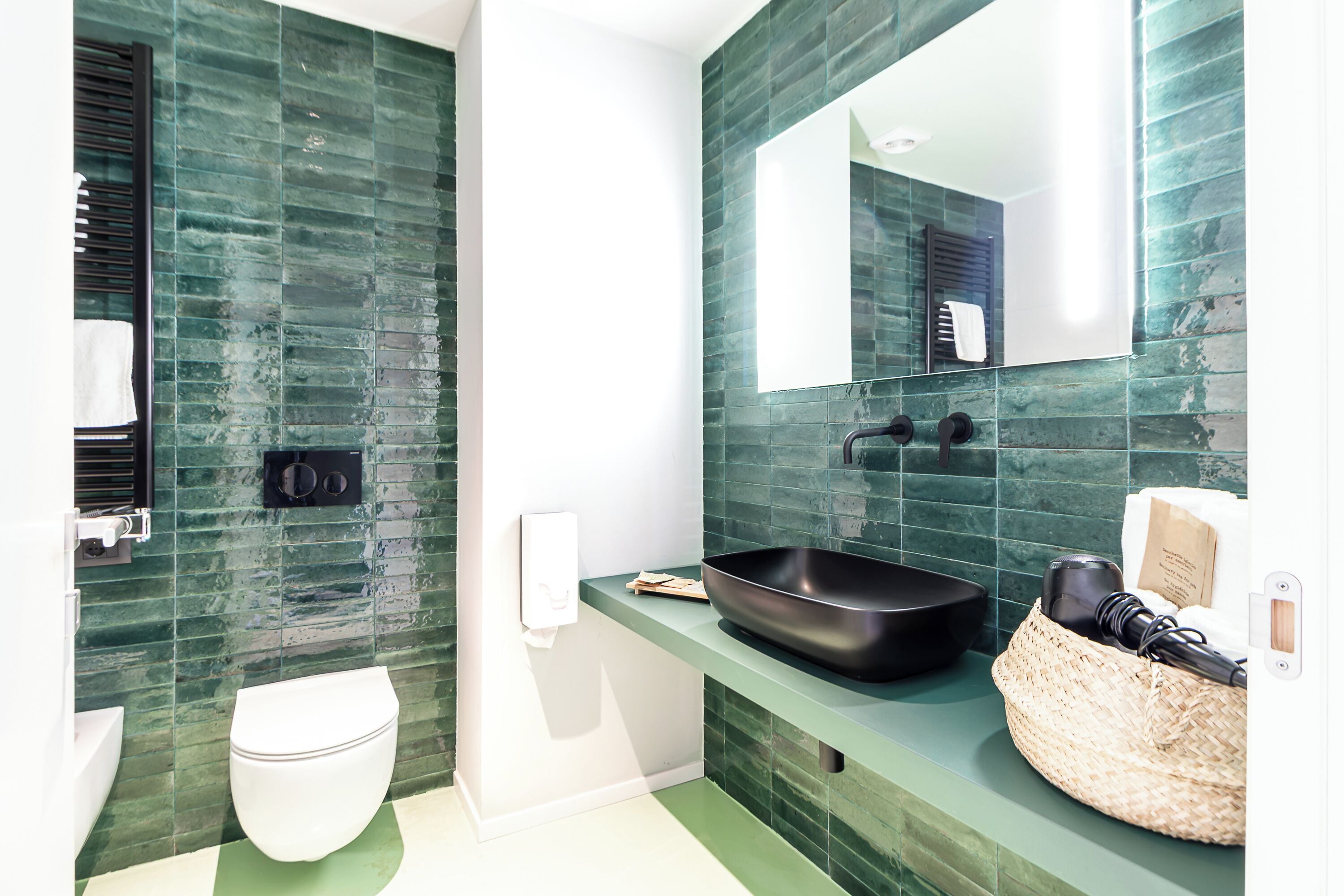 Een moderne badkamer met een groen betegelde wand, een wit toilet, een zwarte wastafel en een spiegel.