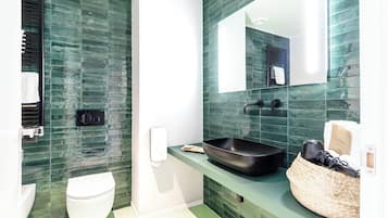 Un baño moderno con pared de azulejos verdes, inodoro blanco, lavamanos negro y espejo.