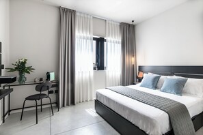 Ett modernt hotellrum med en säng, ett skrivbord, en stol och ett fönster med gardiner.