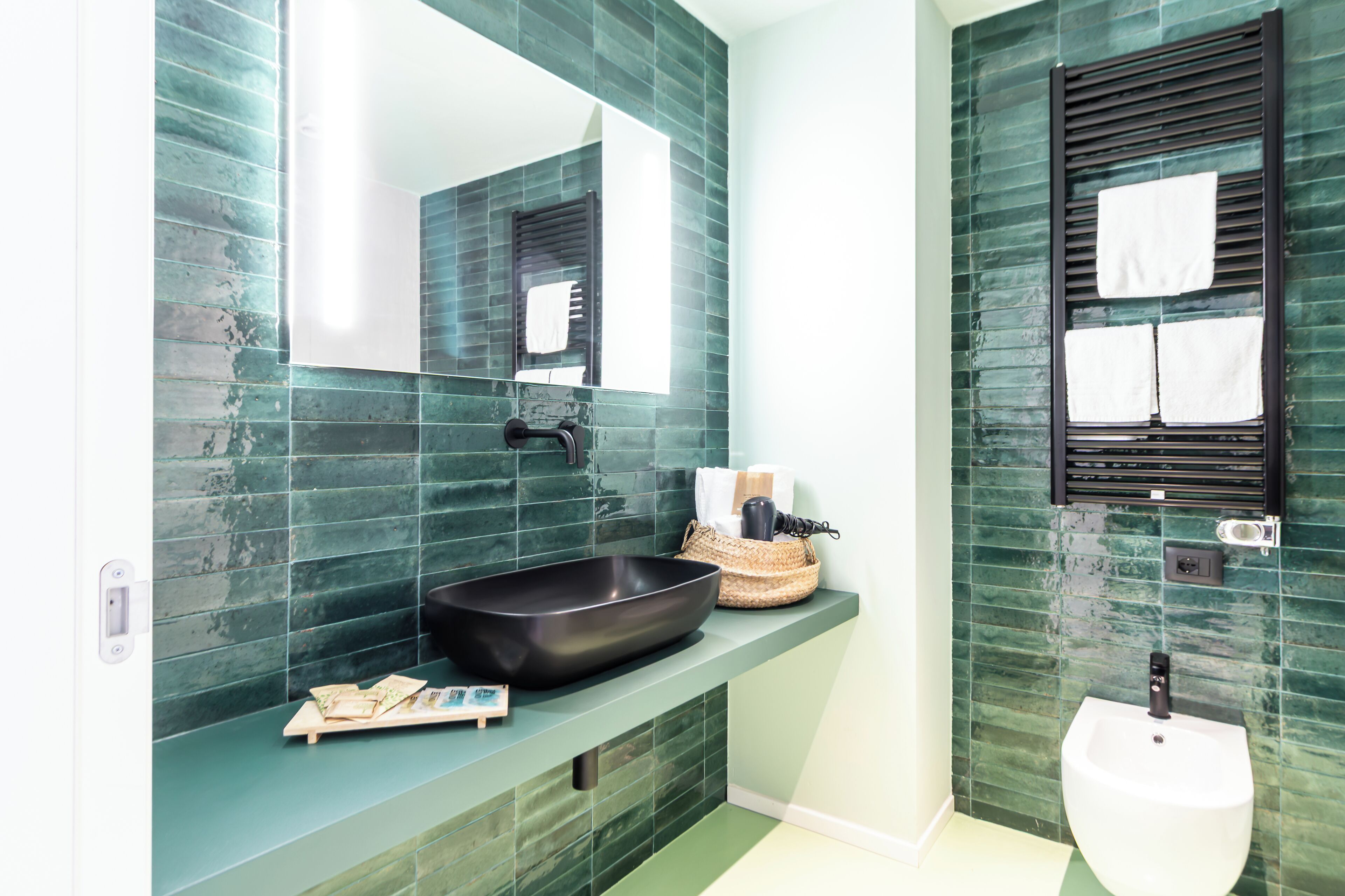 A bathroom with a large mirror, a black basin, a white sink, and a towel rack.
