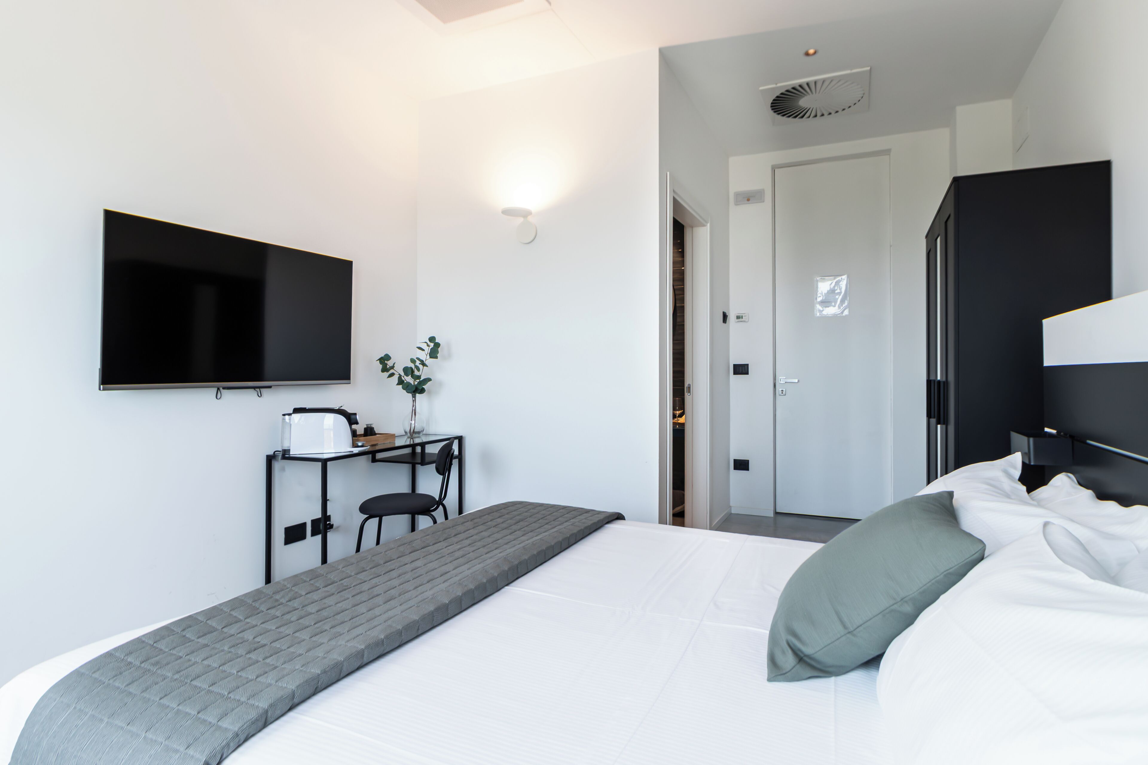 Ein modernes Hotelzimmer mit einem Bett, einem Schreibtisch, einem Sessel, einem Fernseher und einer Tür zu einem weiteren Raum.