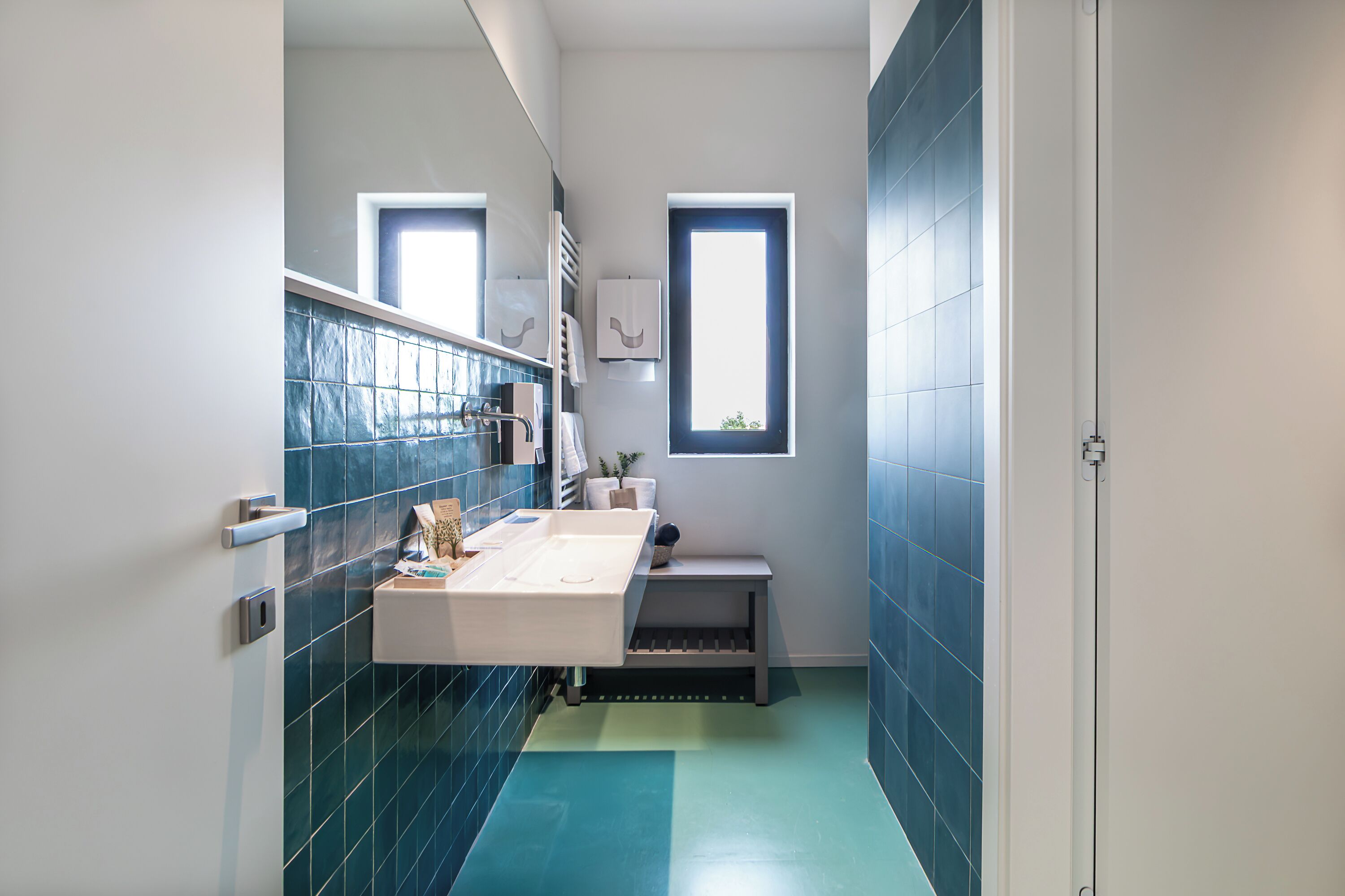 A narrow bathroom with a white sink, blue-tiled walls, and a window.