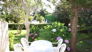 Eine Gartenpatio mit einem runden Tisch und weißen Stühlen, umgeben von üppigem Grün und blühenden Pflanzen.