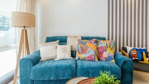 Un salon moderne avec un canapé bleu, des coussins à motifs, une lampe sur pied et un mur à rayures.