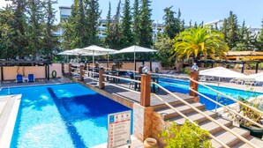 Une piscine avec une terrasse en bois, des chaises longues et des parasols.