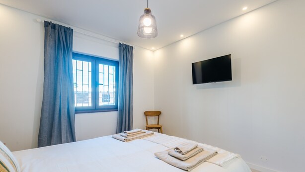 Une chambre d’hôtel avec un lit, une chaise, un téléviseur fixé au mur et une fenêtre avec des rideaux.