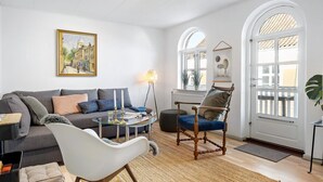 A living room with a sofa, armchair, and coffee table, a painting on the wall, and a window with a view. - 1 bedroom amazing apartment in Mariager (Mariager)