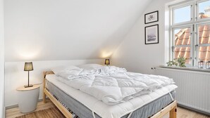 A neatly made bed with white bedding, two bedside lamps, and a window with a view of a tiled roof. - 1 bedroom amazing apartment in Mariager (Mariager)