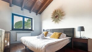 Un dormitorio con una cama grande, una ventana con vistas, un radiador y una mesita de noche con lámpara.