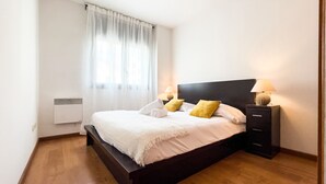 Quarto moderno com cama de madeira, roupa de cama branca e duas luminárias de cabeceira.