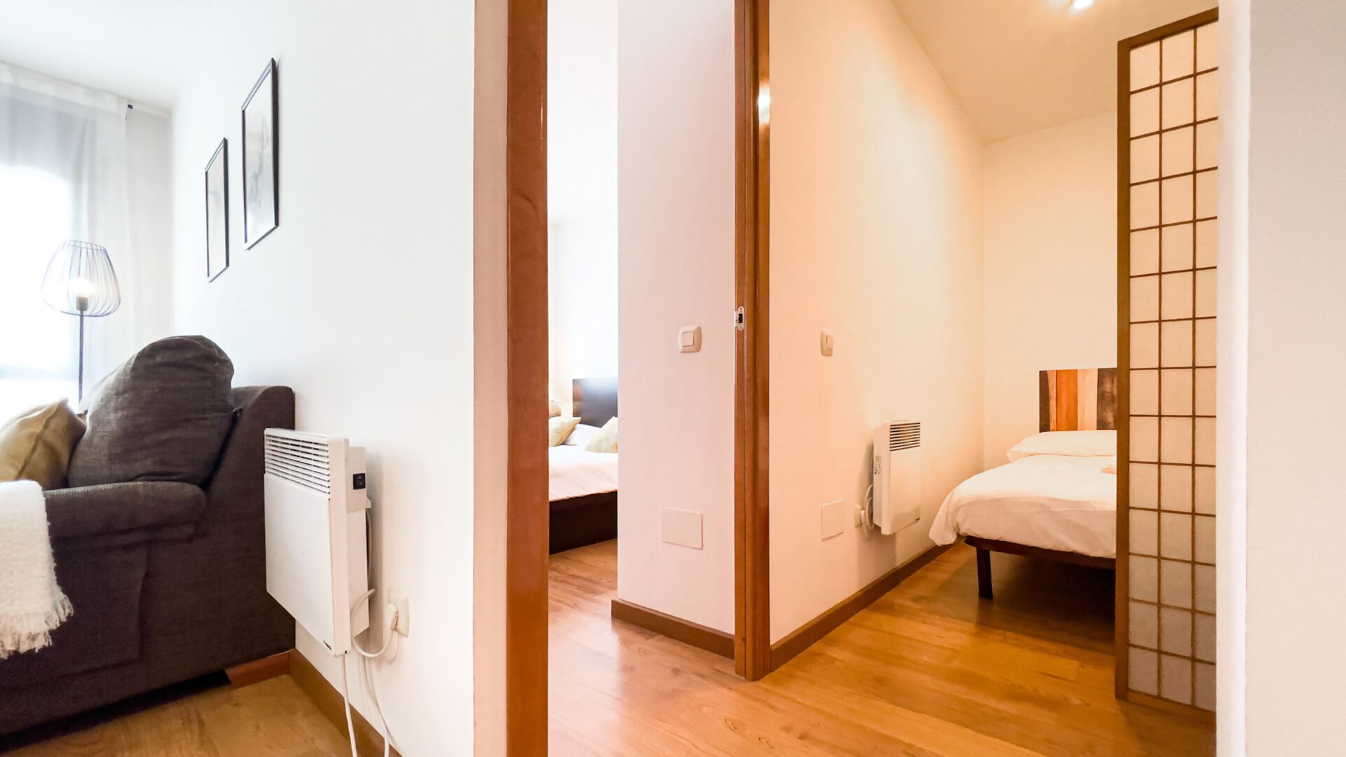 Een hotelkamer met een houten vloer, een bed met wit beddengoed, een nachtkastje en een radiator.