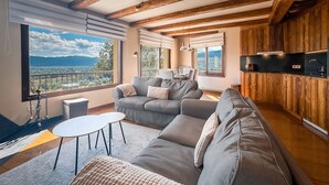 A modern living room with a large sofa, a small round table, and a balcony with a view of the mountains. - Cal Gatesques 1 (Puigcerda)