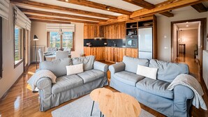 A modern living room with two grey sofas, a wooden ceiling, and a kitchen area with appliances. - Cal Gatesques 1 (Puigcerda)