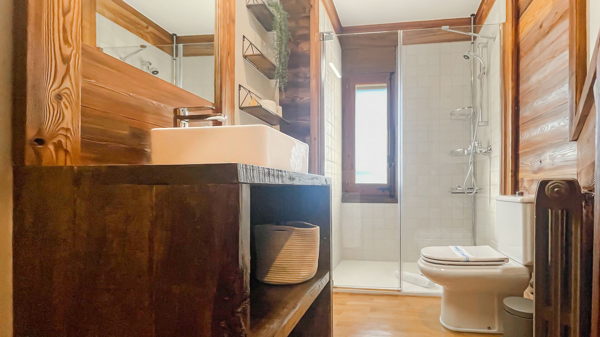 Un baño pequeño con tocador de madera, inodoro y ducha con mampara de vidrio.