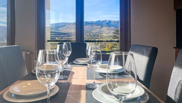 Taula de dinar amb quatre gots de vi i plats, davant d'una finestra que mostra una vista de muntanya.