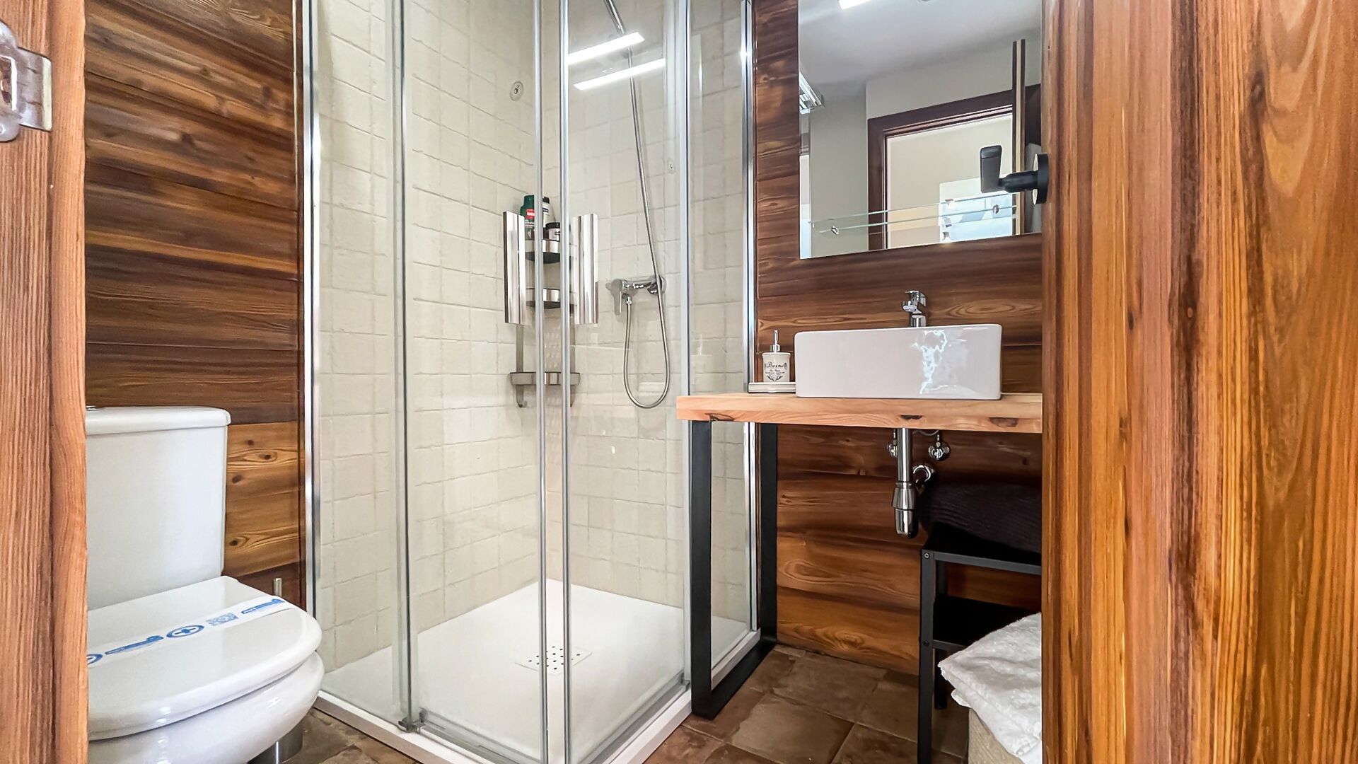 A modern bathroom with a glass-enclosed shower, a white toilet, and a wooden vanity with a sink.