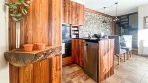 Une cuisine avec des meubles en bois, un mur en pierre et un coin repas comprenant une table et des chaises.