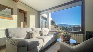 Un salon moderne avec un canapé, une petite table et une vue sur les montagnes, visible à travers de grandes fenêtres.
