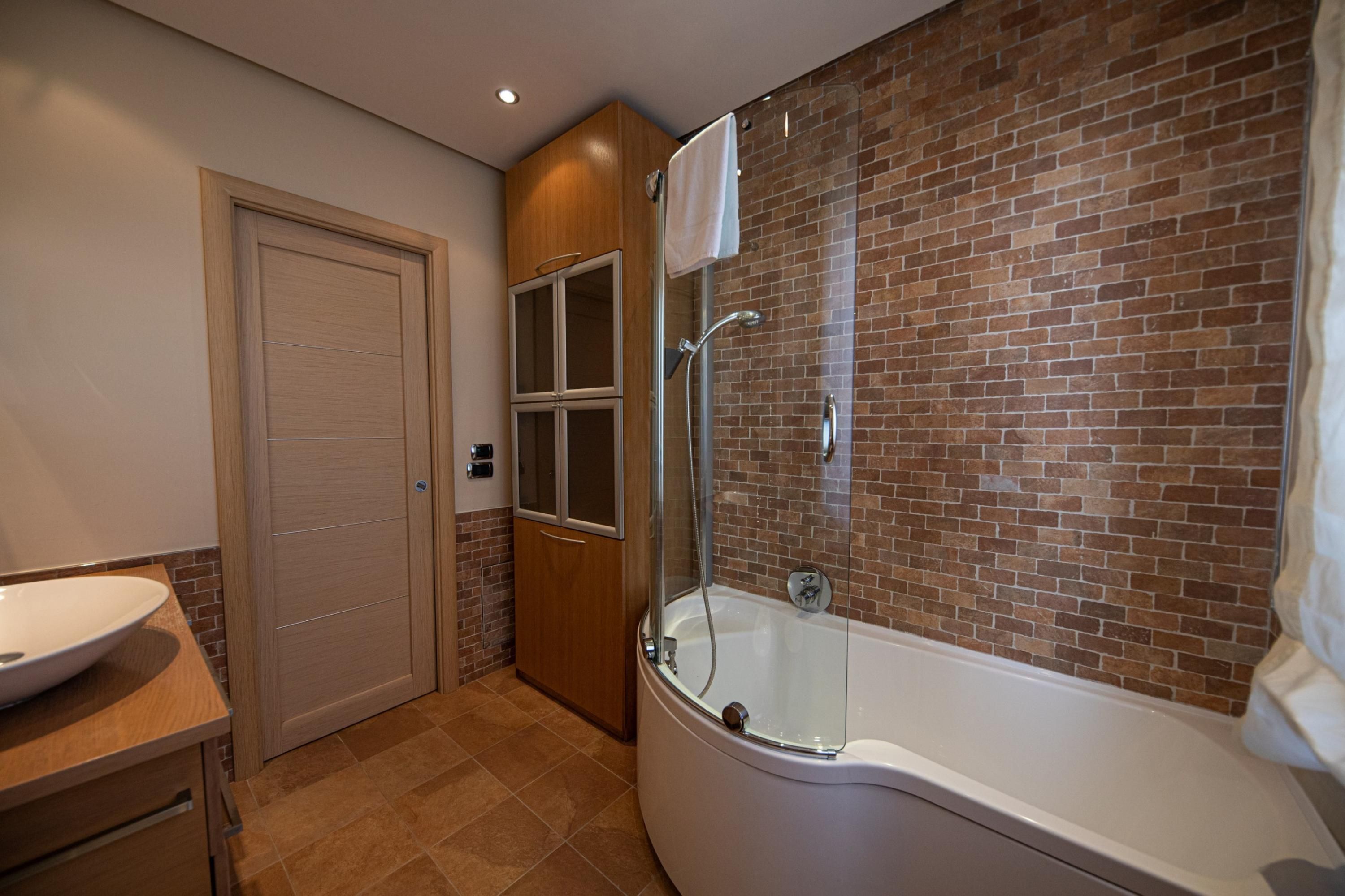 A bathroom with a glass-enclosed shower, a white bathtub, and a wooden vanity with a sink.