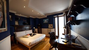 Ein Schlafzimmer mit einem Bett, einem Schreibtisch und einem Stuhl. Es gibt ein Fenster mit Vorhängen, eine Heizung und ein Bild an der Wand.