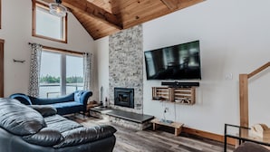 A modern living room with a stone fireplace, a large flat-screen TV, and a blue sofa.