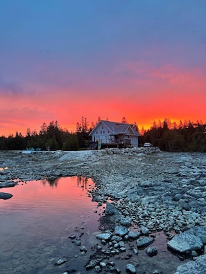 Ett hus vid en bergig flodbank i solnedgången.
