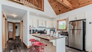A modern kitchen with white cabinets, a stainless steel refrigerator, and a wooden ceiling.