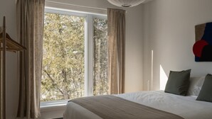 A bedroom with a large window, a bed, a heater, and a wall-mounted artwork.