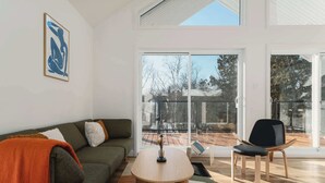 A modern living room with a sofa, a coffee table, and a chair. There is a large window with a view of trees and a deck.