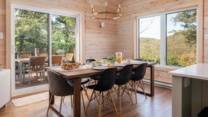 A wooden cabin interior with a dining area, large windows, and a view of the outdoors. - Montagnia escape, Tremblant, Private Spa & Sauna Retreat (Val-des-Lacs)