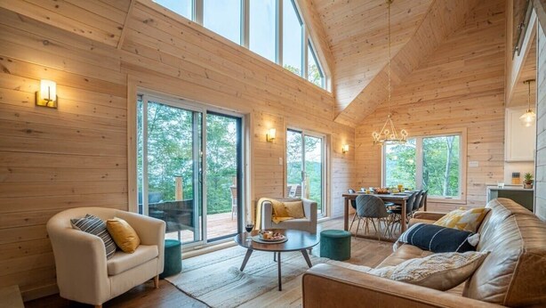 A spacious living room with wooden walls, large windows, and a cozy seating area. - Montagnia escape, Tremblant, Private Spa & Sauna Retreat (Val-des-Lacs)