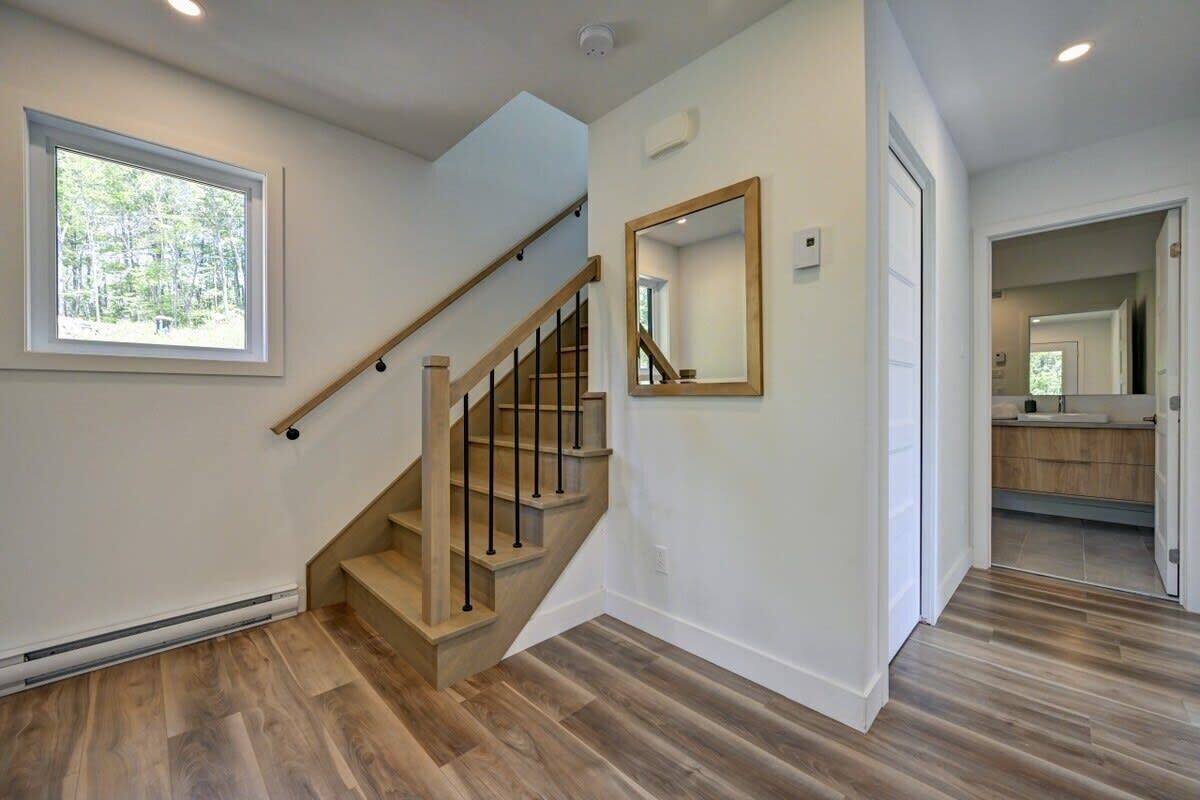 A staircase with wooden steps and black railings, a large window with a view of trees, and a mirror on the wall.