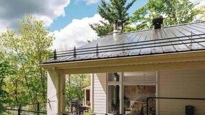 A house with a covered porch, a glass enclosure, and a view of the surrounding greenery. - Chalet w Private Thermal Spa, Nature & Relaxation (Sainte-Béatrix)