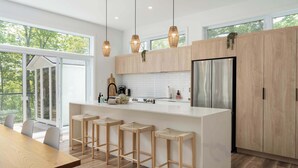 A modern kitchen with a central island, wooden stools, and a large refrigerator. - Chalet w Private Thermal Spa, Nature & Relaxation (Sainte-Béatrix)