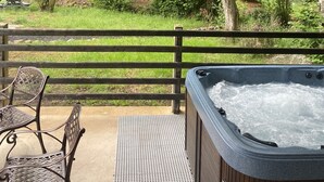 Un espace extérieur aménagé, partiellement abrité, avec un jacuzzi, une terrasse en bois et une vue sur une zone boisée.