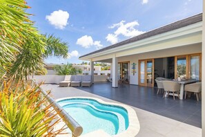 A modern outdoor pool area with lounge chairs and a dining table. - Goudhaen (Jan Thiel)
