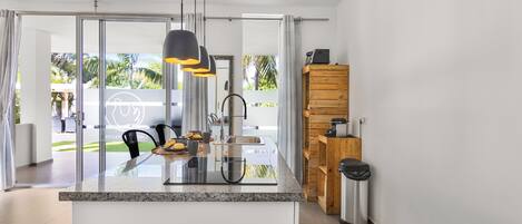 Una cucina moderna con un'isola grande, elettrodomestici in acciaio inossidabile e vista su una zona esterna verdeggiante attraverso porte in vetro.