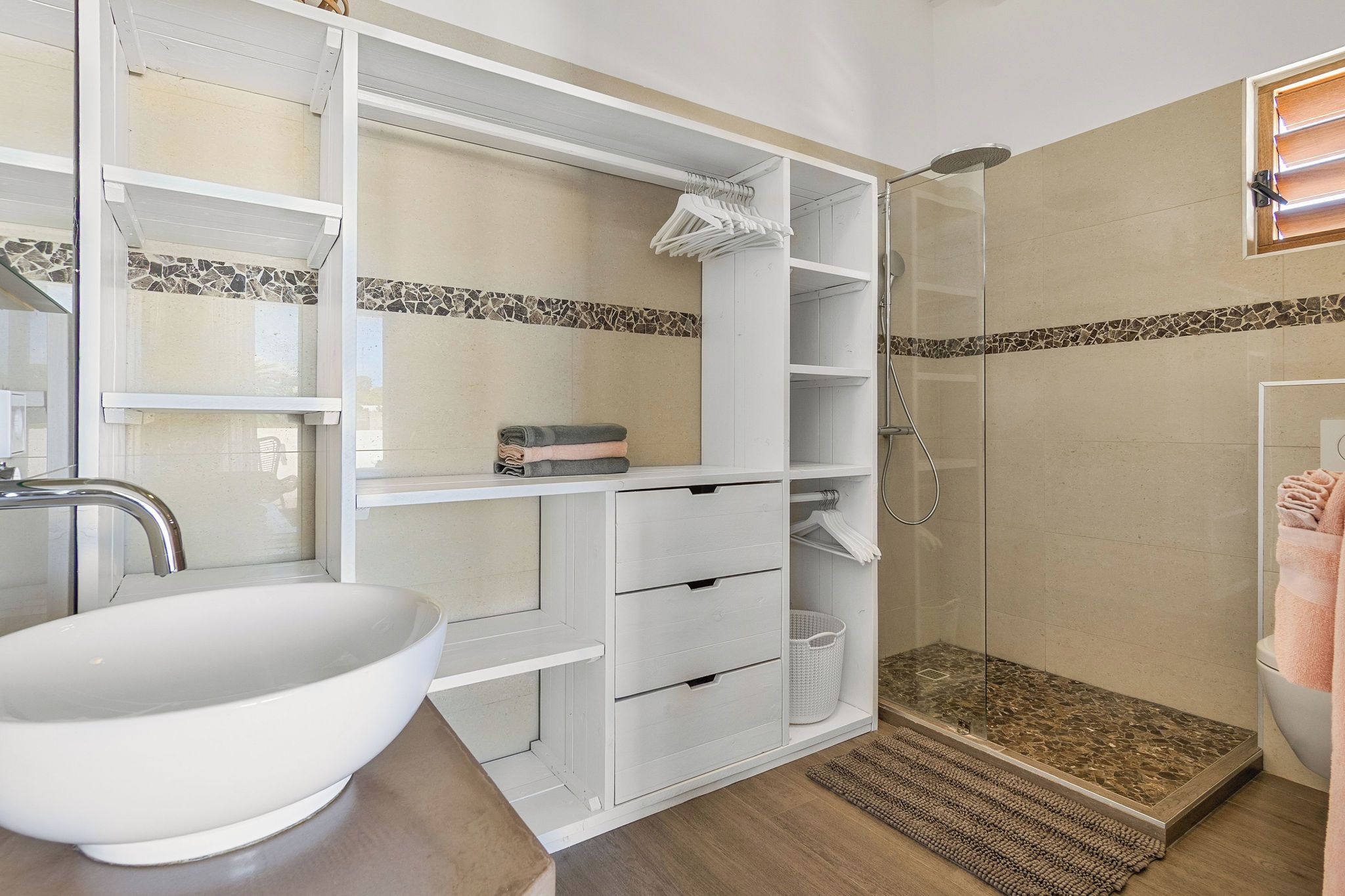 Une salle de bain avec un lavabo blanc, des étagères ouvertes, une douche à l’italienne et un pare-splash carrelé.