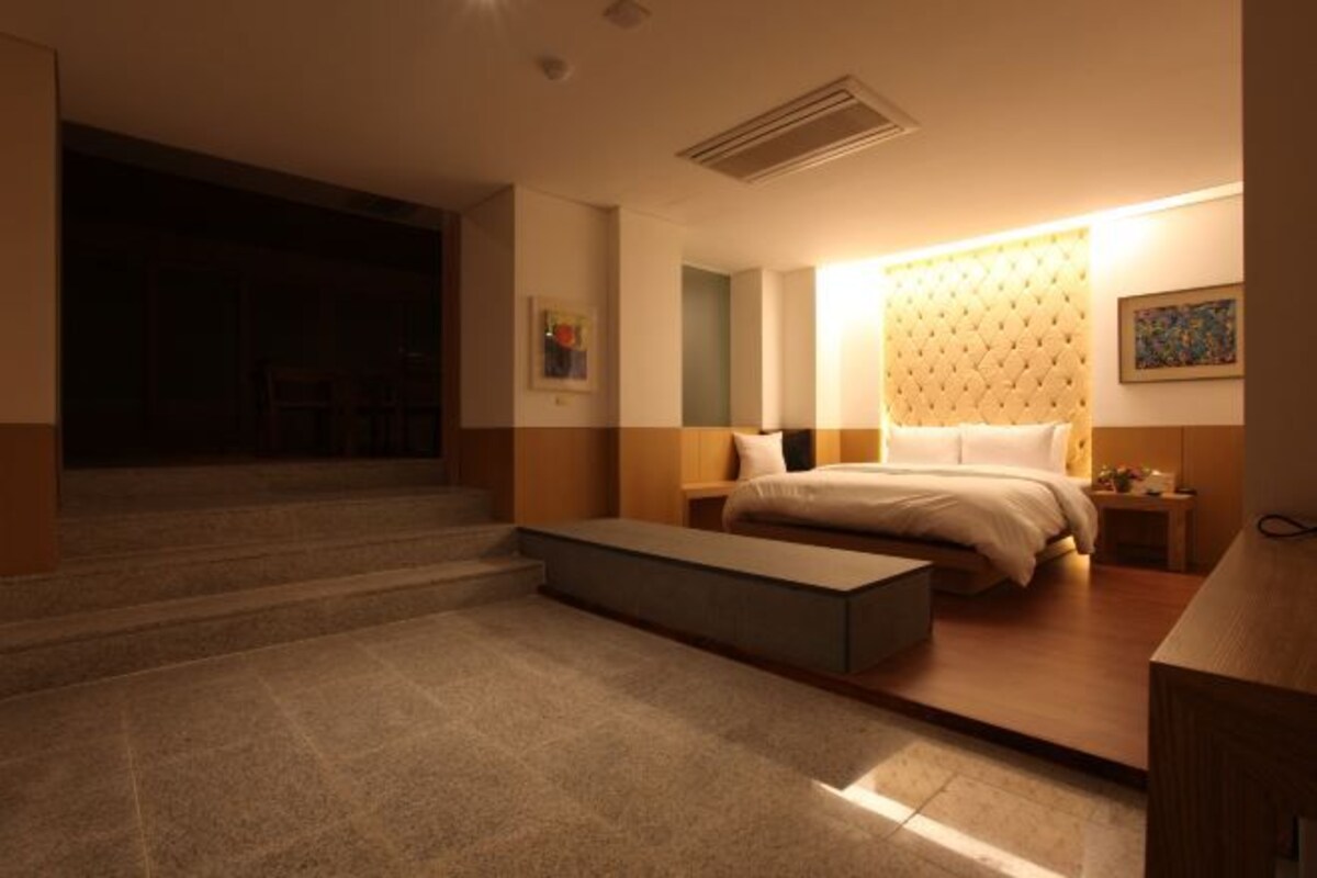 Una habitación de hotel moderna con cama, mesitas de noche, un banco y una escalera que lleva a otra zona.