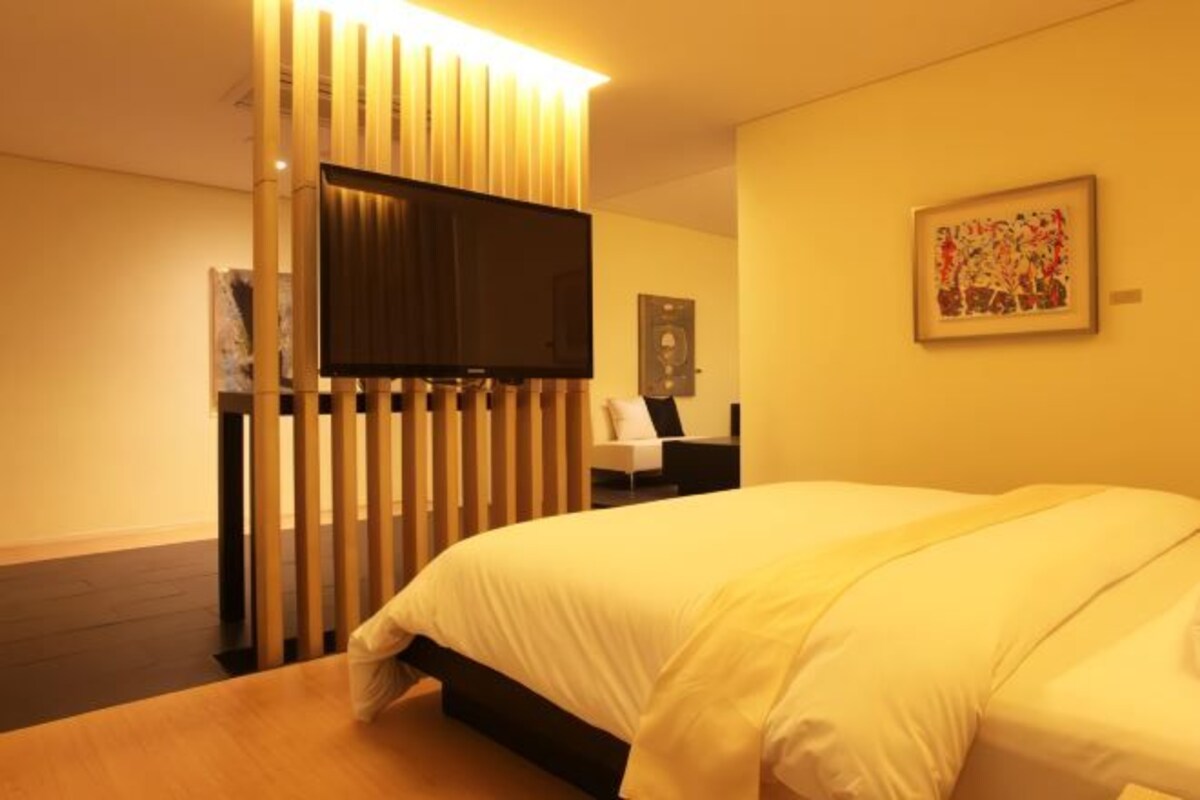Habitación de hotel con cama, televisión instalada en un panel de madera, escritorio con silla y un cuadro en la pared.