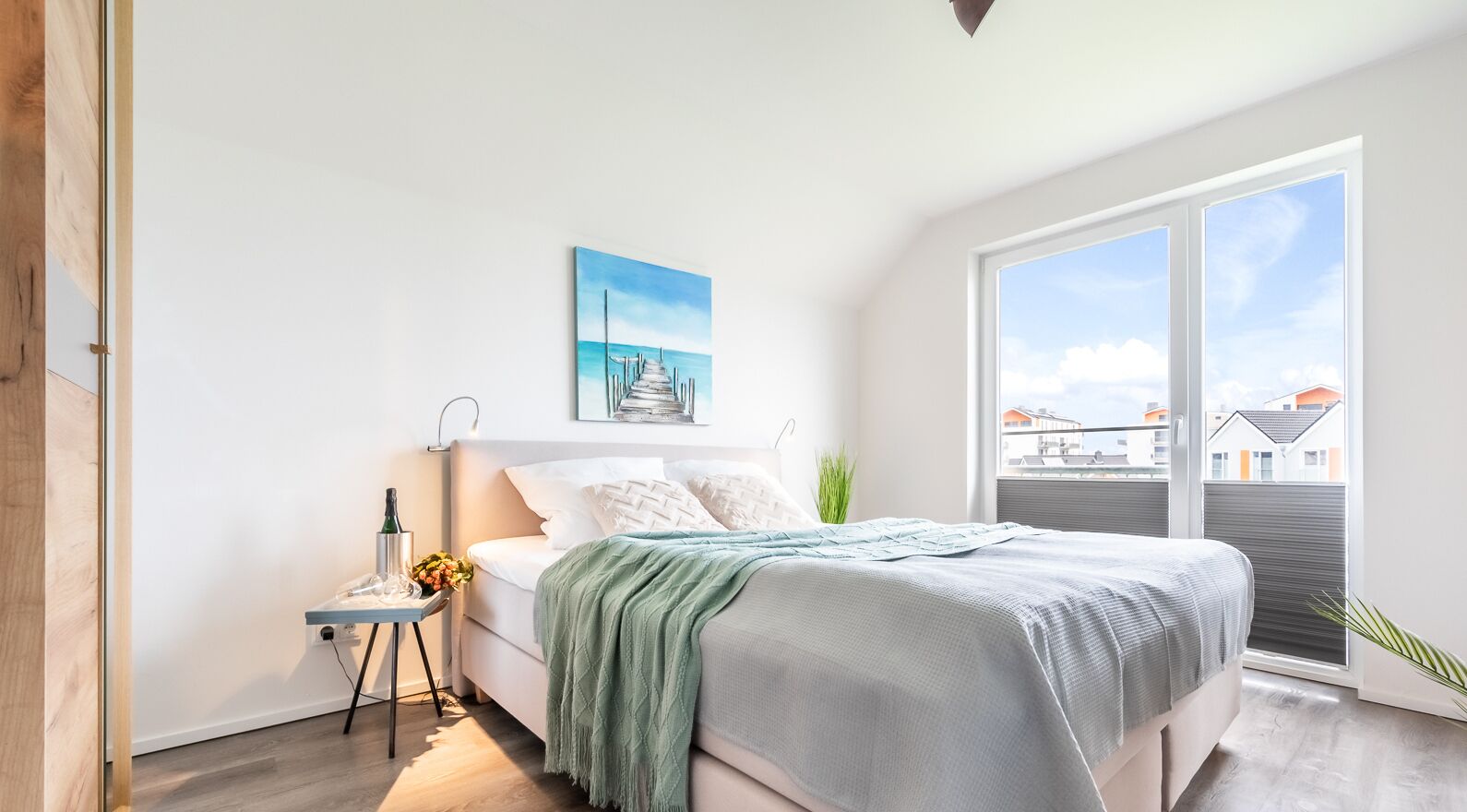 A bedroom with a bed, a nightstand, a painting, and a large window.