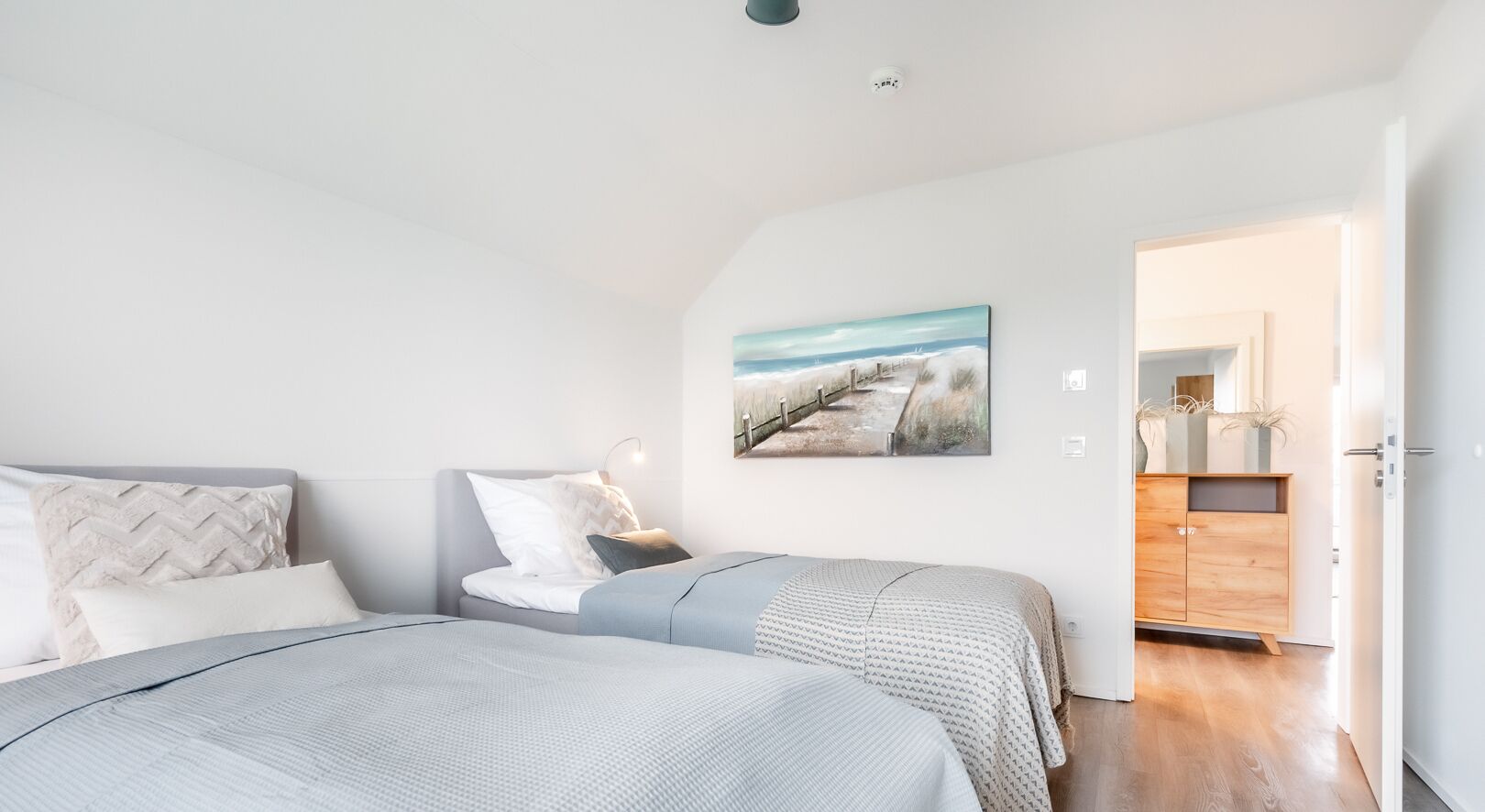 Ein Schlafzimmer mit zwei Betten, einem Bild an der Wand und einer Holzkommode im Hintergrund.