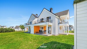 Une maison à deux étages dotée d’un balcon, d’une terrasse couverte et d’une pelouse bien entretenue.