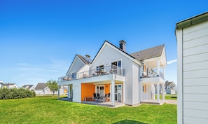 A two-story house with a balcony, a covered patio, and a well-maintained lawn.