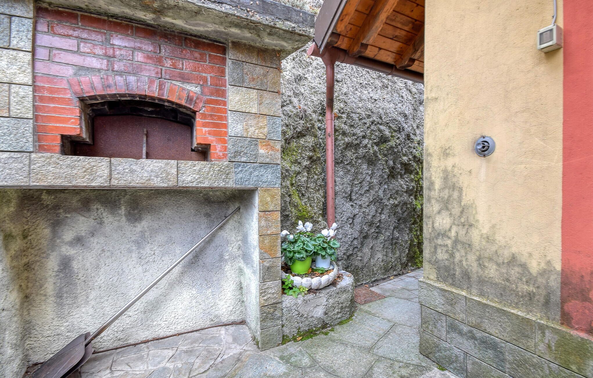 Ein schmaler Steinweg führt zu einem Backsteinhaus mit einem kleinen Fenster und einem Blumentopf.