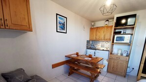 Un espace de vie compact comprenant une table à manger en bois, une kitchenette équipée d’un four à micro-ondes et d’une machine à café, ainsi qu’un lit recouvert d’une couverture à motifs.