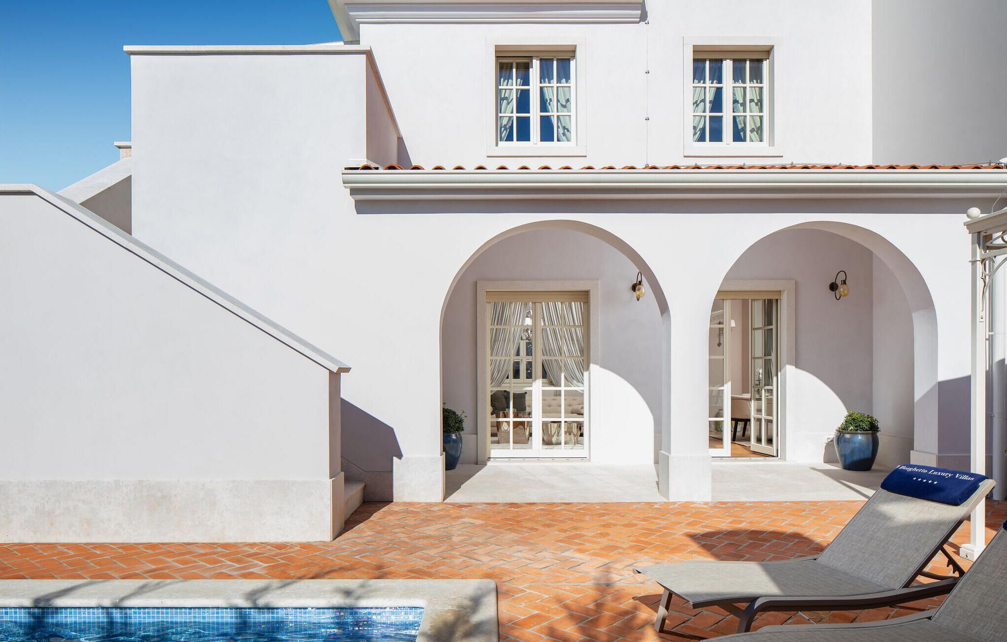 Un bâtiment blanc doté d’une piscine, de deux portes en arc de cercle et d’un fauteuil de relaxation.