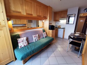 A compact kitchen with wooden cabinets, a dining table, and a sofa with patterned cushions.