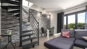 Ein modernes Wohnzimmer mit Treppe, einer Couch, einem Esstisch und Blick ins Freie.